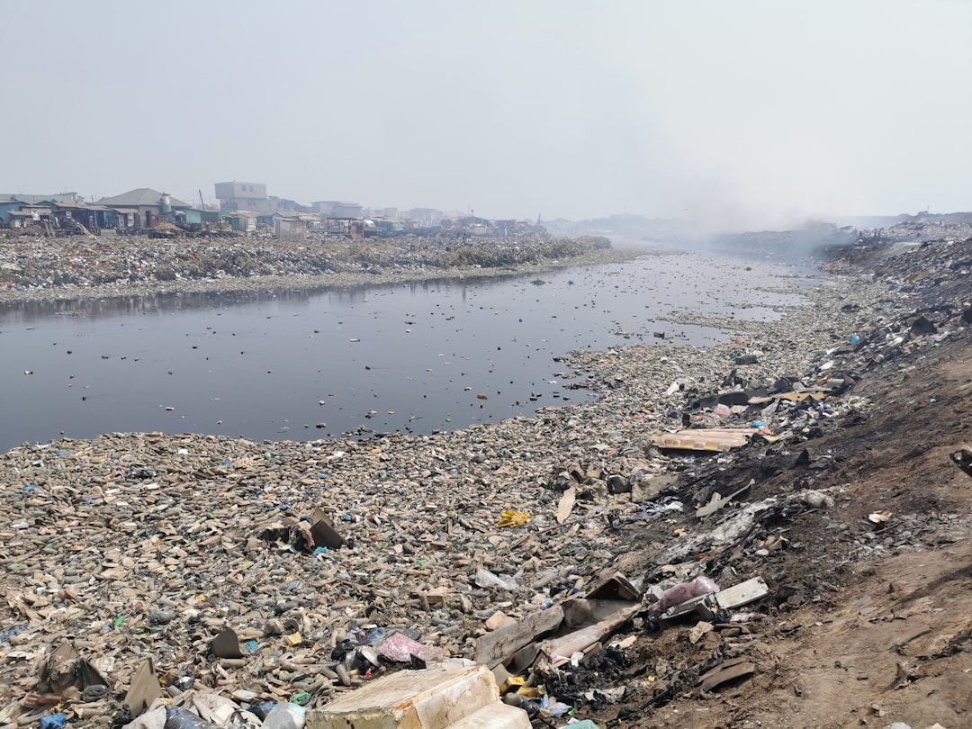 E-waste impact on environment shown by polluted river filled with discarded electronics and plastic waste near community.