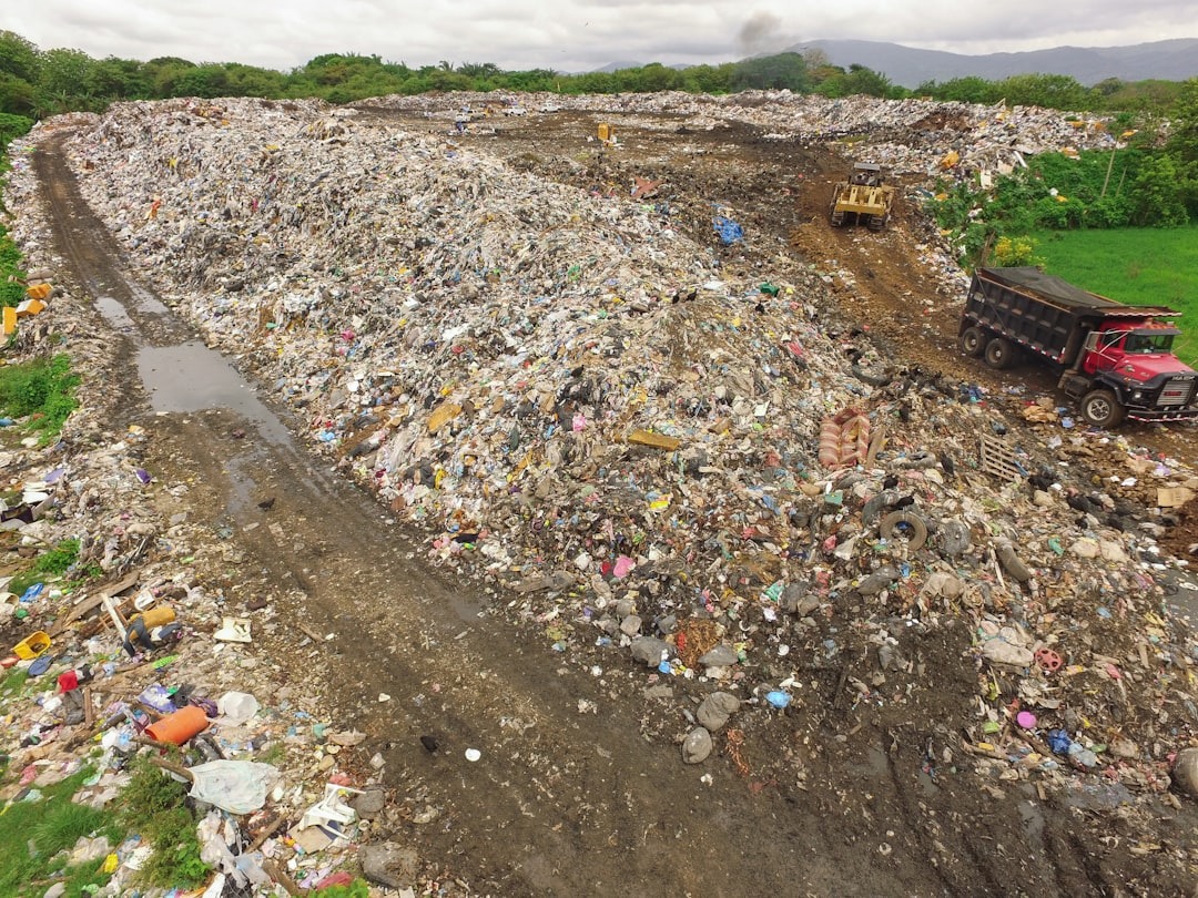 E-waste impact on environment with massive landfill site and garbage trucks dumping electronic and household waste.